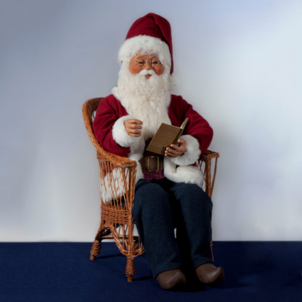 Santa Claus sitting in a chair, reading a book.